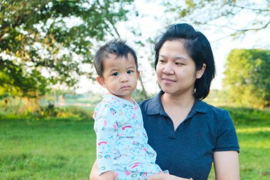 Ypung Asyalı anne, küçük bebeğini parkın açık hava tatiline kusuyor.