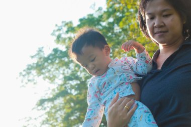 Ypung Asyalı anne, küçük bebeğini parkın açık hava tatiline kusuyor.