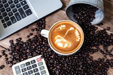 Diz üstü bilgisayarı ve hesap makinesi çalışma alanı manzaralı ahşap masadaki sıcak latte sanat kahvesi.