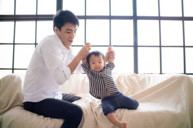 Küçük Asyalı çocuk babasıyla sıcak odada ilk adım pratiği yapıyor.