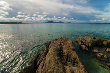Bulutlu, güneşli, deniz manzaralı, kayalık bir deniz manzarası.