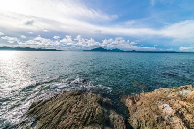 Bulutlu, güneşli, deniz manzaralı, kayalık bir deniz manzarası.