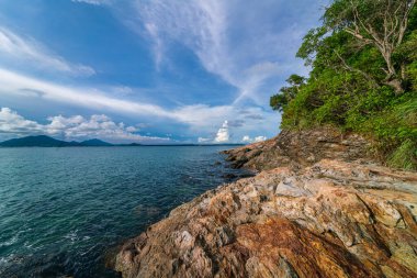 Bulutlu, güneşli, deniz manzaralı, kayalık bir deniz manzarası.
