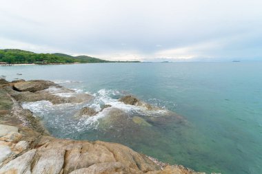 Bulutlu, güneşli, deniz manzaralı, kayalık bir deniz manzarası.