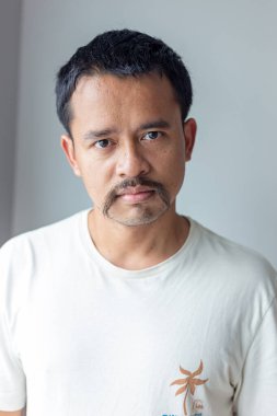 Yakışıklı Asyalı adam gri arka planda gülümsüyor ve gülüyor.