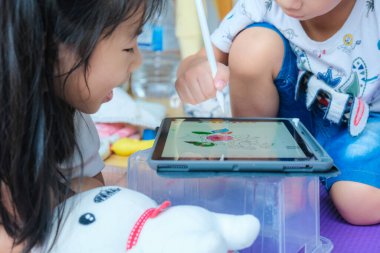 Anaokulu çocuğu ve kız çocuğu rahat bir odada tabletle resim çiziyorlar.