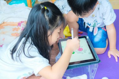 Anaokulu çocuğu ve kız çocuğu rahat bir odada tabletle resim çiziyorlar.