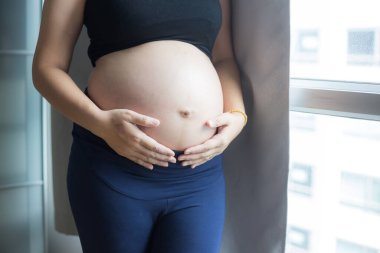 Mutlu gülümseyen pragnant Asyalı kadın rahat bir odada yeni doğan bebek konseptini umuyor.
