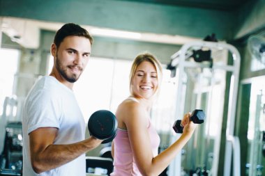 Erkek ve kadın, Fitnes Spor Salonu 'nda dambılla çalışıyor. Erkek arkadaşıyla spor yapıyor.