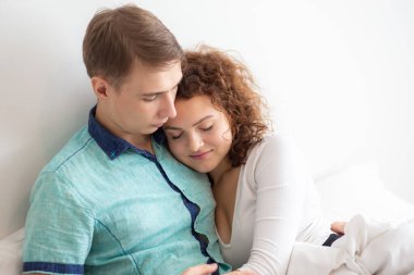 Aşk çifti sabah beyaz yatakta uzanıyor. Mutlular ve birbirlerine sarılıyorlar. Sevginin rahatlığı.