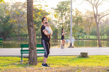 Asya 'lı sporcu anne parkın gün batımında çocuk istirahatgahında açık hava aktivitesi düzenliyor.