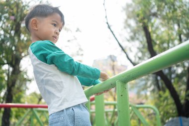 Mutlu Asyalı çocuk oyun parkına tırmanıyor. Açık hava aktivitesi.