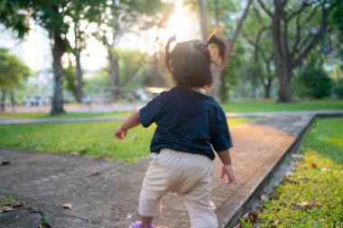 Küçük sevimli Asyalı kız yeşil çimlerde yürüyor halk parkında güneş doğarken