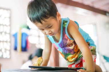 Tablet oynayan sevimli küçük çocuk evde çizgi film izliyor.