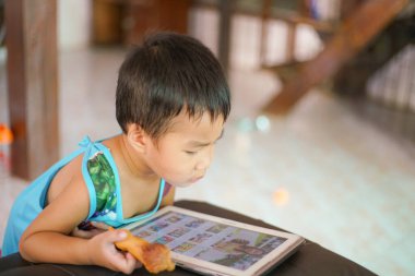 Tablet oynayan sevimli küçük çocuk evde çizgi film izliyor.