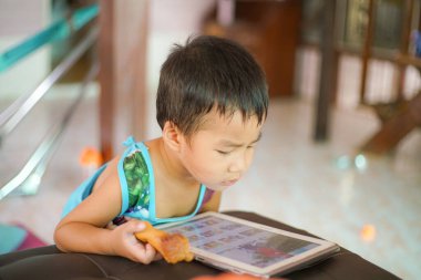 Tablet oynayan sevimli küçük çocuk evde çizgi film izliyor.