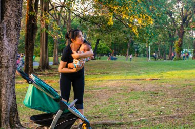 Asyalı anne, çocuk arabasıyla çocuk parkında gezintiye çıkmış.