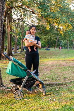 Asyalı anne, çocuk arabasıyla çocuk parkında gezintiye çıkmış.