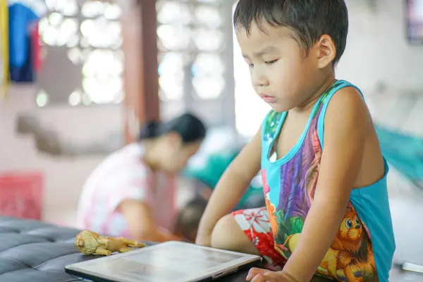 Tablet oynayan sevimli küçük çocuk evde çizgi film izliyor.