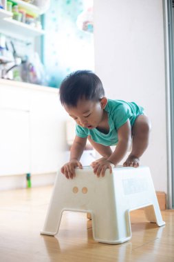 Sevimli küçük çocuk, rahat bir odada beyaz tabureye tırmanıyor.