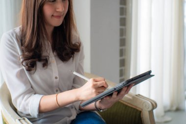 Mutlu Asyalı iş kadını dijital tablet kullanıyor yatak odasındaki koltukta oturuyor, perde arkasında, boşluğu kopyalıyor.