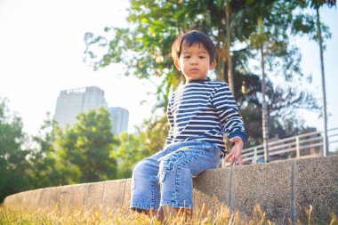 Yeşil çimenlerde oturan mutlu Asyalı çocuk bitkilerin doğasıyla oynuyor.