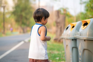 Genç Asyalı çocuk çevreyi temizleyip çöpleri parktaki bir çöp kutusuna atıyor.