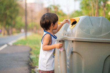 Genç Asyalı çocuk çevreyi temizleyip çöpleri parktaki bir çöp kutusuna atıyor.