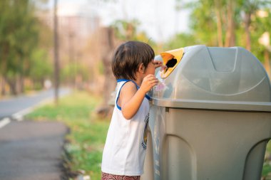 Genç Asyalı çocuk çevreyi temizleyip çöpleri parktaki bir çöp kutusuna atıyor.