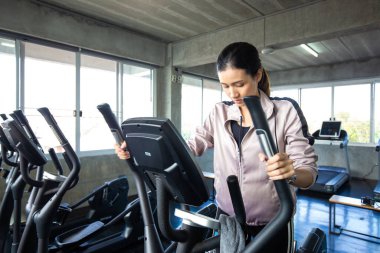 Spor salonundaki spor salonunda eliptik makine üzerinde çalışan Asyalı kadın.