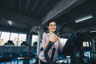 Spor salonundaki eliptik makine üzerinde çalışan Asyalı kadın, kardiyo egzersizi.