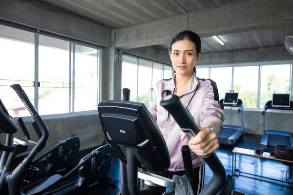 Sport asian woman working out on elliptical machine in fitness room cardio exercise