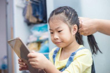 Sevimli Asyalı liseli kız, evde annesinin yanında giyinirken tablet bilgisayar kullanıyor.