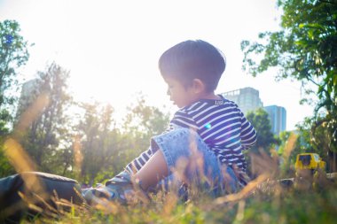 Yeşil çimenlerde oturan mutlu Asyalı çocuk bitkilerin doğasıyla oynuyor.