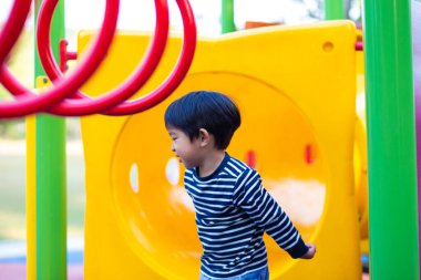 Küçük Asyalı çocuk oyun parkında kayıyor ve kıpır kıpır mutlu çocuk.