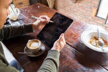 Adam, çalışma masası olan bir ahşap üzerinde dijital boş tablet ekranını gösterir