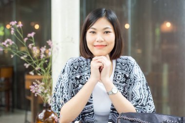 Güzel Asyalı kadın kafede oturuyor, gülümsüyor ve kameraya bakıyor.