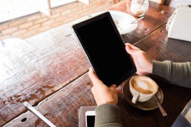 İnsan eli tablet boş ekranı ahşap masada sıcak latte ile kullanır, Arka görünüm eli kapat