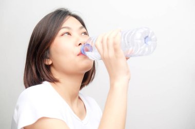 Beyaz arka planda izole edilmiş şişeden su içen genç Asyalı kadın.