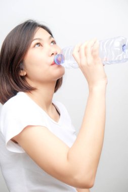 Beyaz arka planda izole edilmiş şişeden su içen genç Asyalı kadın.