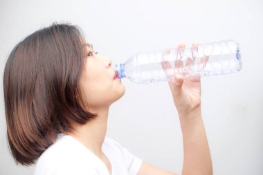 Beyaz arka planda izole edilmiş şişeden su içen genç Asyalı kadın.
