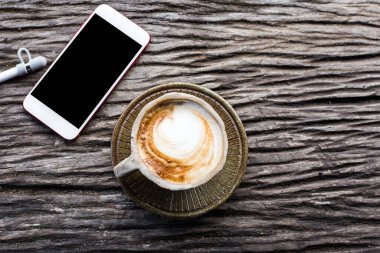 Ahşap arka planda bir fincan kahveli akıllı telefon. 