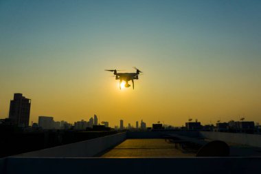 Gün batımında şehrin üzerinde uçan kuadkopter silueti.