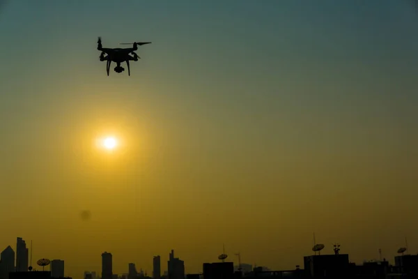 Silhouette of quadcopter flying over the city at sunset