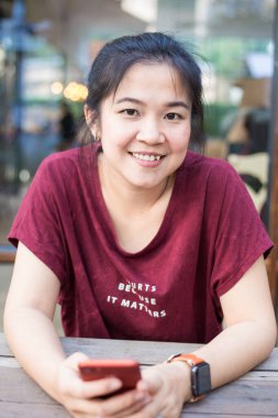 Kafede oturan Asyalı kadın akıllı telefon kullanıyor.