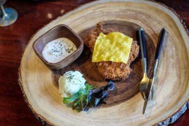 Tavuklu biftek, dilimlenmiş peynir salatası ve ahşap tabak manzarası.
