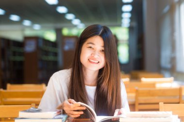 Ahşap masada oturan Kütüphane kitap ile düşünme mutlu Asya öğrenci genç kadın