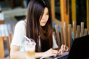 Bir kafede otururken telefon iletişim ile taşınabilir dizüstü bilgisayar kullanan iş kadını.