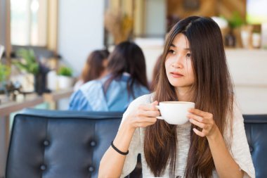 Asyalı öğrenci kadın çekici genç fincan kahve içecek kafe kitaplığında tutun.