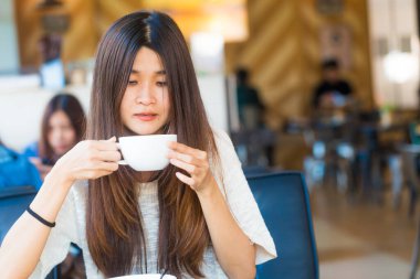 Asyalı öğrenci kadın çekici genç fincan kahve içecek kafe kitaplığında tutun.